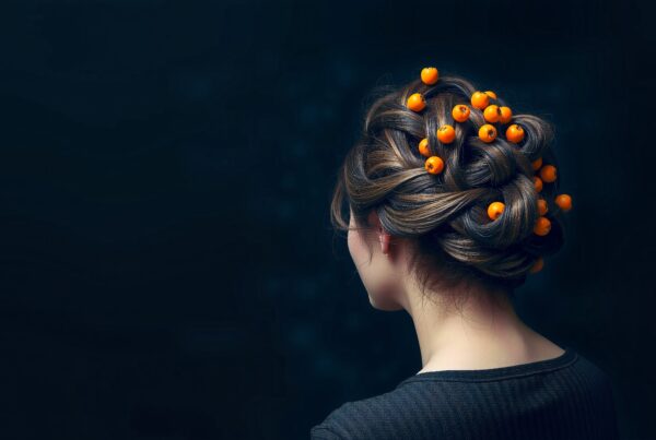 A woman with an intricate updo decorated with orange berries against a dark background.