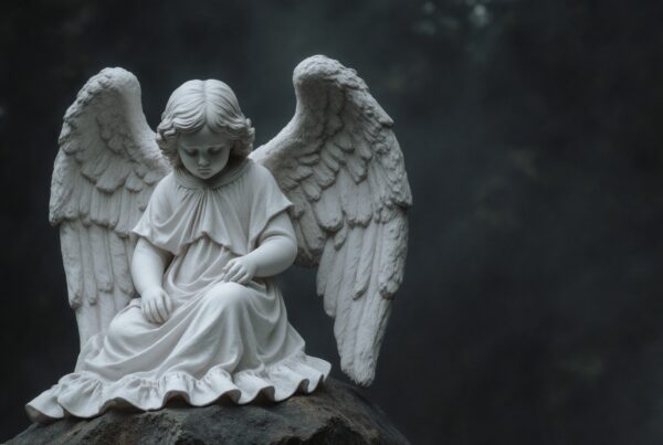 A peaceful angel statue sits thoughtfully with detailed wings against a misty, dark background.