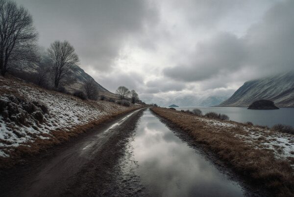 Dirt road through snowy landscape with cloudy sky.