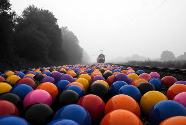 A vibrant array of multicolored balls on a railway track with a distant train, creating a striking contrast in a foggy landscape.