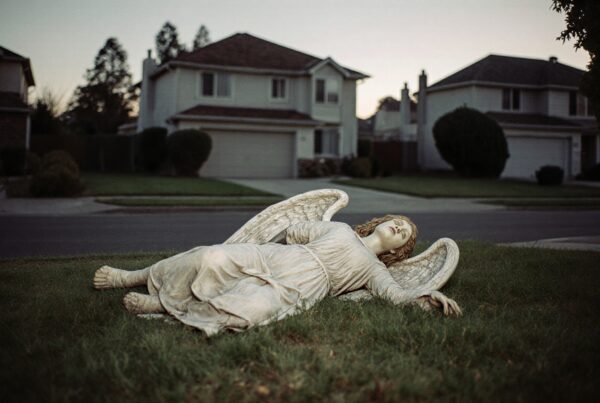 A serene angel statue lies on grass in a suburban neighborhood surrounded by houses.