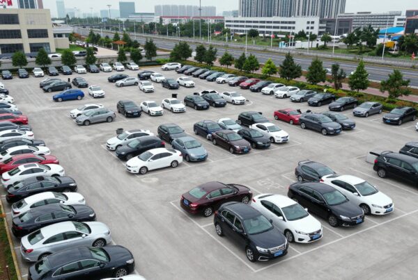 A well-organized urban parking lot filled with various cars and surrounded by tall buildings and greenery.