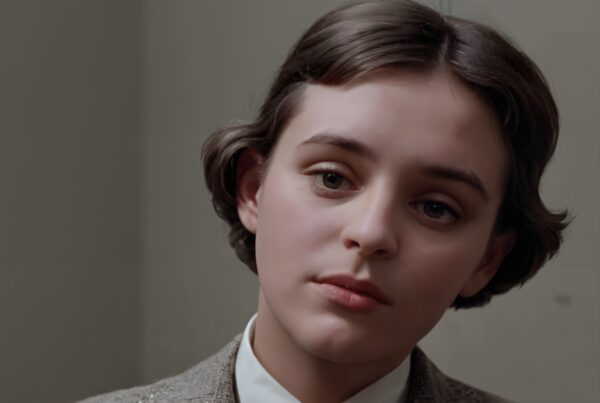Close-up portrait of young person with contemplative expression, elegant attire in neutral background.
