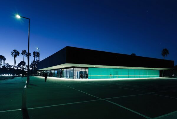 Modern rectangular building at twilight with ambient lighting, surrounded by palm trees, and a tranquil setting.