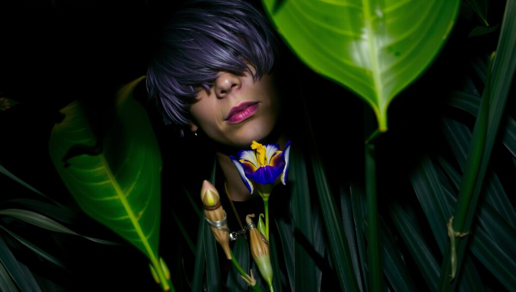 Purple-hair figure partially hidden by lush tropical foliage wit