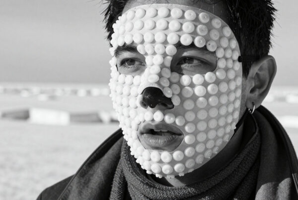 Man wears beaded mask on snowy background, artistic black and white portrait
