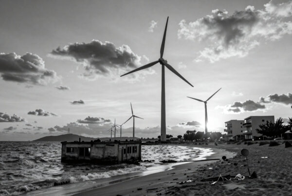Black and white photo showing wind turbines near decaying seaside structures and waves crashing ashore