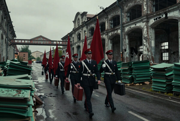 Soldiers carrying flags and suitcases walk down rainy alley between ruined factories