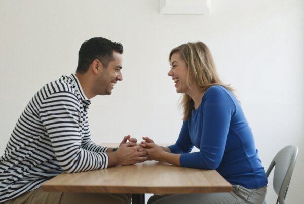 A man and woman happily conversing while holding hands across a table, wearing casual clothing, in a minimalistic setting.