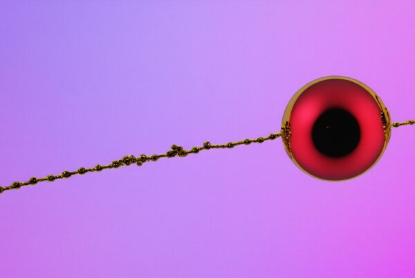 A spherical red object with a gold chain on a purple-pink gradient background.