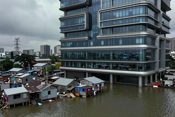 Large glass building by stilt houses showcasing urban poverty.