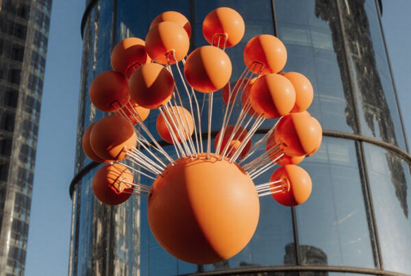 A large orange spherical sculpture against a glass building in an urban setting.