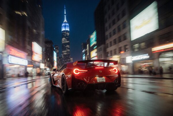Red sports car speeding through city street at night with vibrant neon lights and towering skyscraper in rainy urban setting.