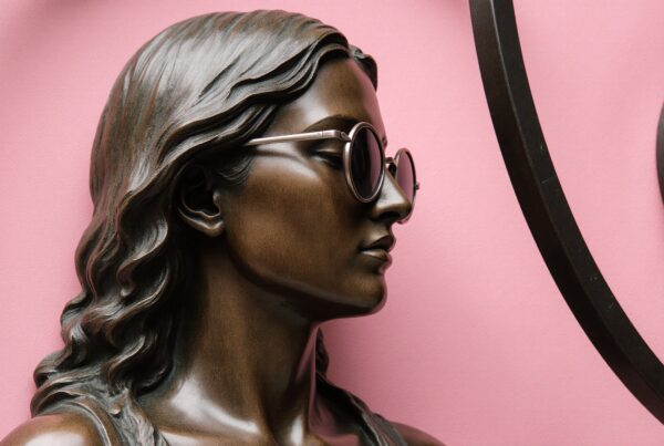 Bronze sculpture with sunglasses against pink background.