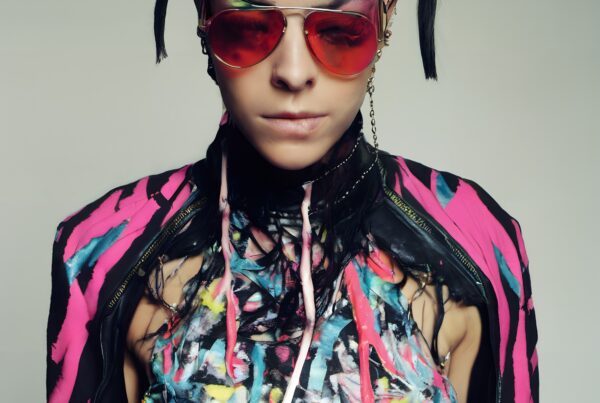 Stylish individual in vibrant outfit with red sunglasses and bold piercings.