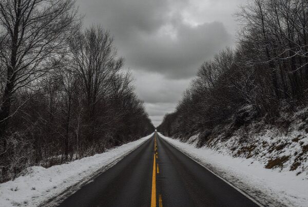 A long straight road through snow-covered trees under a gray winter sky.