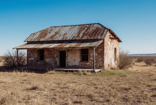 Weathered brick house in vast, dry landscape with blue sky.
