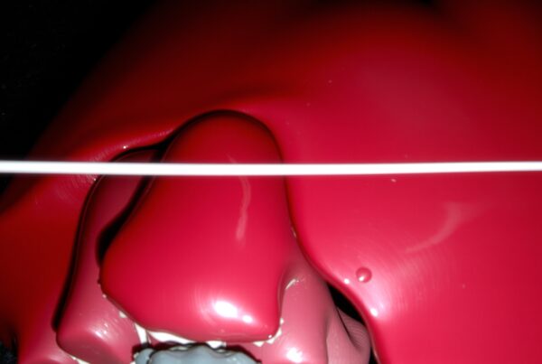 Close-up of a glossy red heart sculpture with a white rod crossing above on a dark background.