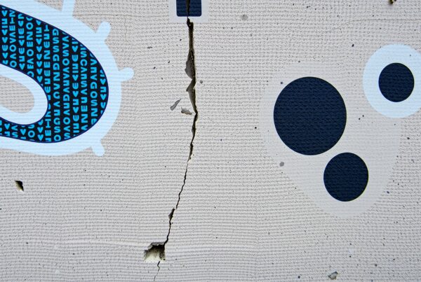 Abstract mural art on textured concrete wall showing geometric patterns with a central crack.