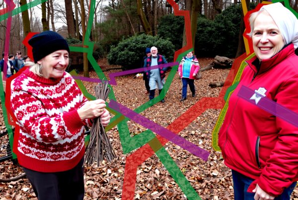 A group of people in a forest, collecting sticks, with multicolored geometric lines overlaying the scene.