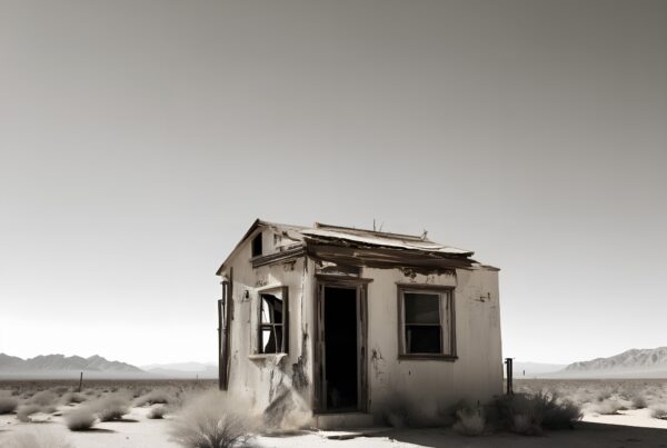 Abandoned shack in a desolate desert landscape with a backdrop of distant mountains under a brooding sky.