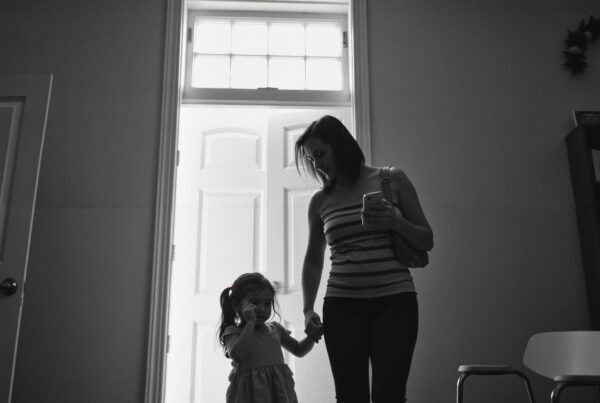 A woman and child stand in a doorway, with light from outside highlighting their silhouettes.